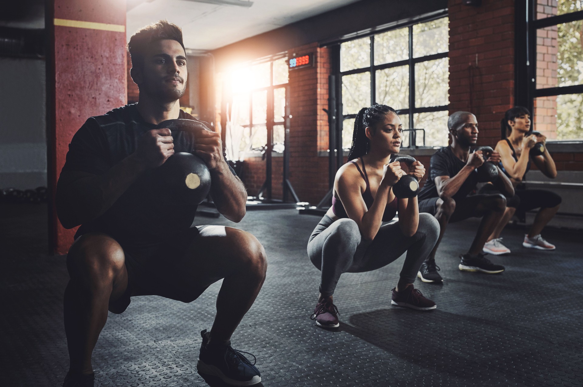 Group, fitness and workout with kettlebell to squat in class for muscle, wellness or healthy body. Team, exercise and strong people weightlifting for power, bodybuilding and training together at gym